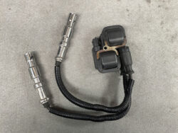 Automotive ignition coil pack with two coil modules and two spark plug boots on a concrete surface.
