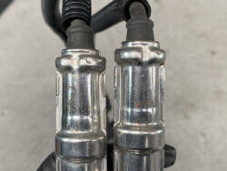 Close-up of two metal quick-connect fittings labeled 2 and 1 with black cables entering from above, against a gray background.