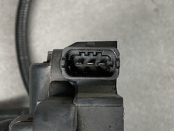 Close-up of a black three-pin electrical connector socket with metal contacts, mounted on a gray automotive component.
