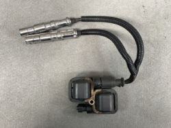 Twin automotive ignition coil pack with two spark plug boots and wiring harness on a gray work surface