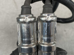 Two metal quick-connect fittings side by side, connected by black hoses, with stamped numbers on the chrome surfaces.
