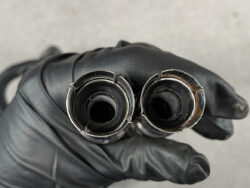 Close-up of a gloved hand holding two worn metal cylindrical tubes with jagged rims.