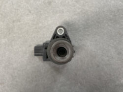 Close-up of a black automotive sensor with a circular rubber opening and a side electrical connector on a gray background, viewed from above.