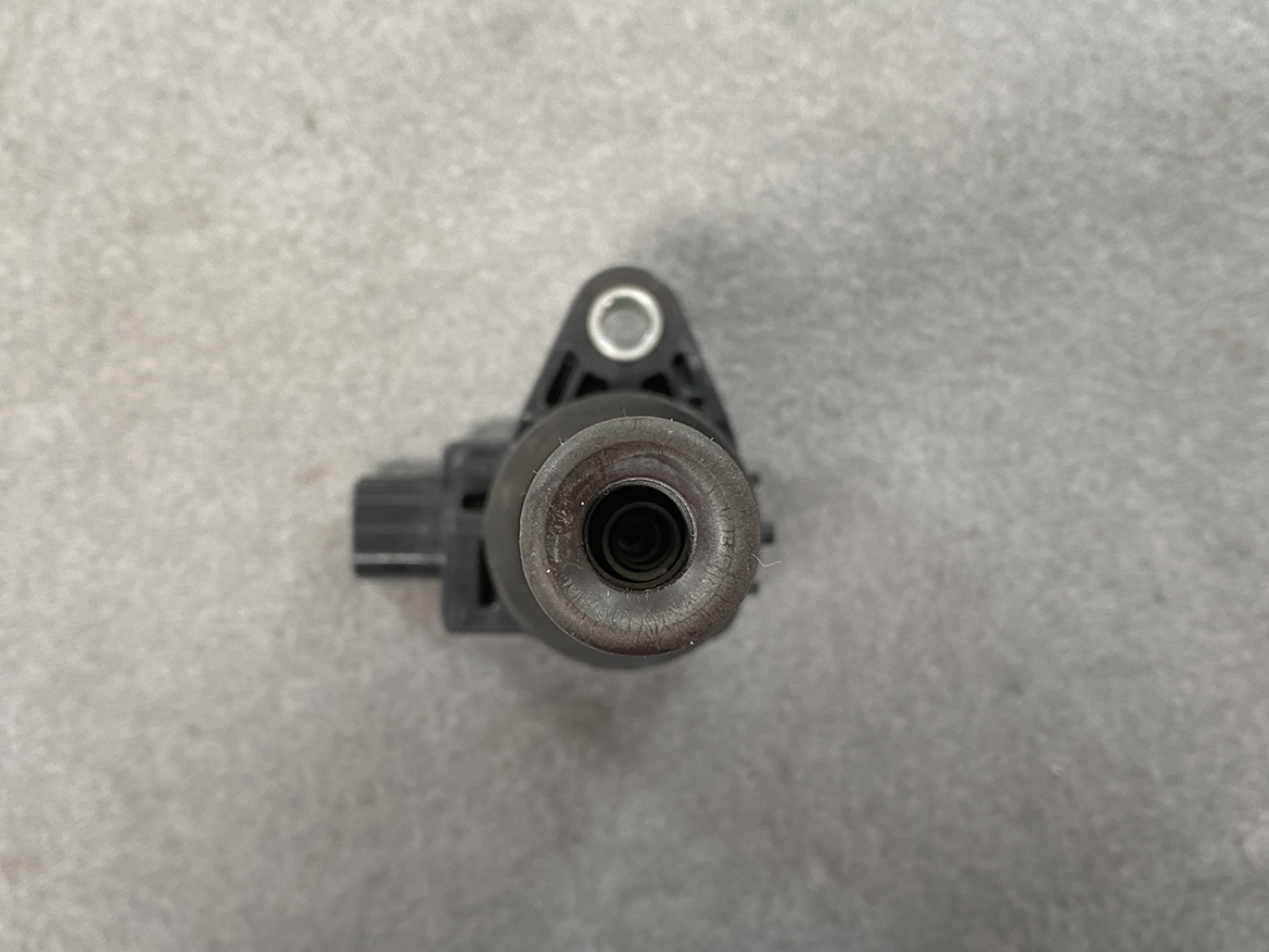 HON-COIL-CM11-116_5 HONDA Genuine IGNITION COIL CM11-116 / L-series Engine » NZ.95 » JDM-PARTS NZ » JDM-PARTS NZ Close-up of a black automotive sensor with a circular rubber opening and a side electrical connector on a gray background, viewed from above. HONDA Genuine IGNITION COIL CM11-116 / L-series Engine » JDM-PARTS NZ