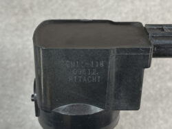 Close-up of a black plastic component marked 'CM1-118', '09612', Hitachi, with a circular mounting base underneath.