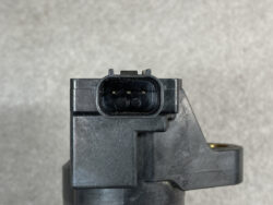 Close-up of a black automotive electrical connector with two metal pins inside a rectangular housing on a gray plastic module.