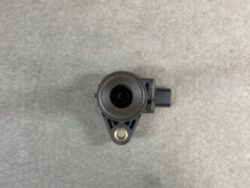 Automotive camera module with a circular lens in a black plastic housing mounted on a small bracket on a gray surface