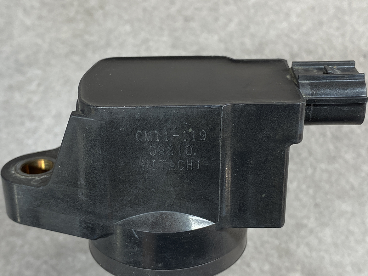 HON-COIL-CM11-119_2 HONDA Genuine IGNITION COIL CM11-119 / L-series Engine » NZ.95 » JDM-PARTS NZ » JDM-PARTS NZ Close-up of a black automotive sensor with mounting hole and connector, stamped CM11-19 09610 Hitachi. HONDA Genuine IGNITION COIL CM11-119 / L-series Engine » JDM-PARTS NZ