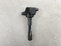 Vehicle ignition coil with connector on top and rubber boot at bottom on a gray surface.