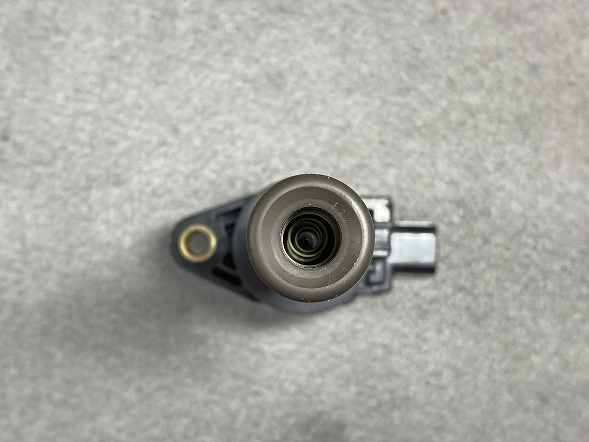 HON-COIL-CM11-119_5 HONDA Genuine IGNITION COIL CM11-119 / L-series Engine » NZ.95 » JDM-PARTS NZ » JDM-PARTS NZ Top-down view of a cylindrical automotive sensor or connector with a circular opening, mounted on a black plastic housing on a gray surface. HONDA Genuine IGNITION COIL CM11-119 / L-series Engine » JDM-PARTS NZ
