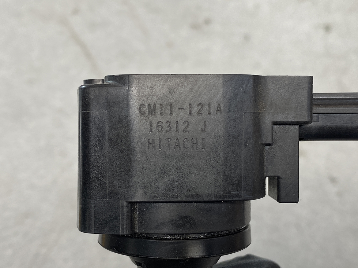 HON-COIL-CM11-121A_2 HONDA Genuine IGNITION COIL CM11-121A / L-series Engine » NZ.95 » JDM-PARTS NZ » JDM-PARTS NZ Close-up of a black Hitachi CM11-12IA component with stamped model numbers on a plastic housing. HONDA Genuine IGNITION COIL CM11-121A / L-series Engine » JDM-PARTS NZ