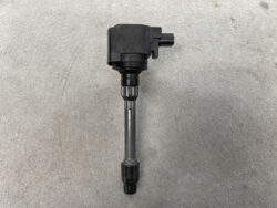 Automotive ignition coil with electrical connector on top and spark plug boot at bottom, laid on concrete surface