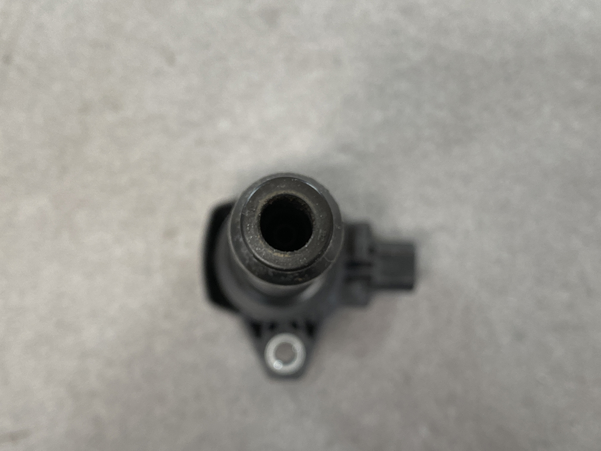 HON-COIL-CM11-121A_5 HONDA Genuine IGNITION COIL CM11-121A / L-series Engine » NZ.95 » JDM-PARTS NZ » JDM-PARTS NZ Close-up of a black cylindrical nozzle with a hollow center, viewed from above on a gray surface. HONDA Genuine IGNITION COIL CM11-121A / L-series Engine » JDM-PARTS NZ