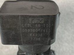 Close-up of a black automotive component with a FoMoCo stamp and stamped codes: LF2L18 100°, 099700-1468, K4238, 1206, on a dark surface.