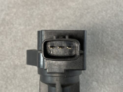 Three-pin black automotive connector with gold pins inside an oval housing, viewed head-on on a gray surface.