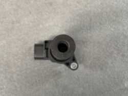 Top-down view of a black plastic automotive component with a hollow cylindrical opening and a mounting tab with a circular metal bushing to the side.