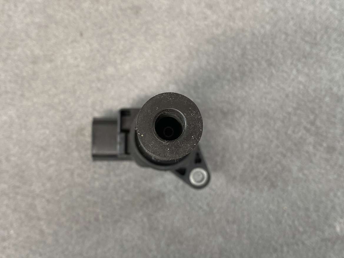 MAZ-COIL-LF2L_5 MAZDA Genuine IGNITION COIL K4238 / LF2L-18-100 / LF, L3 Engine » NZ.95 » JDM-PARTS NZ » JDM-PARTS NZ Top-down view of a black plastic automotive component with a hollow cylindrical opening and a mounting tab with a circular metal bushing to the side. MAZDA Genuine IGNITION COIL K4238 / LF2L-18-100 / LF, L3 Engine » JDM-PARTS NZ