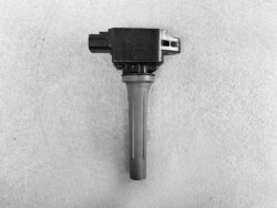 Automotive ignition coil with spark plug boot on a gray textured surface, shown from the side for identification.