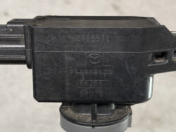 Close-up of a black Mazda automotive module with embossed diagram and serial numbers on its surface.