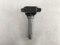 Ignition coil pack with a gray boot and electrical connector, photographed on a beige surface.