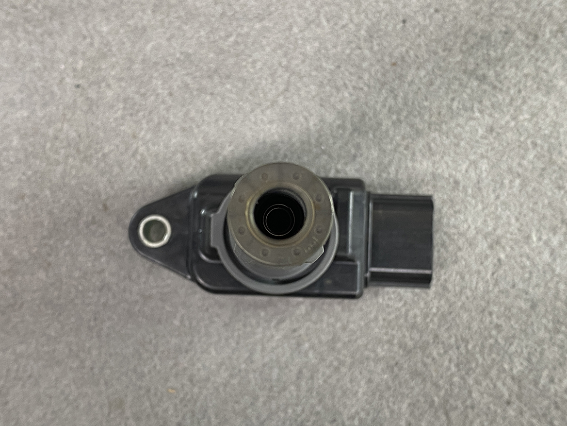 MAZ-COIL-P51R18100_5 MAZDA Genuine IGNITION COIL H6T15571 / P51R-18-100 SKYACTIV-G » NZ.95 » JDM-PARTS NZ » JDM-PARTS NZ Close-up of a black automotive electrical component with a circular metal ring and a rectangular connector, placed on a gray surface. MAZDA Genuine IGNITION COIL H6T15571 / P51R-18-100 SKYACTIV-G » JDM-PARTS NZ