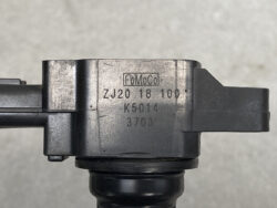 Close-up of a dark metal mechanical housing with stamped markings including 'FoMoCo' and serial numbers ZJ20 18 100, K5014, 3703