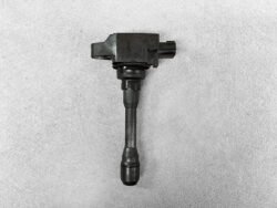 Automotive ignition coil with electrical connector on top, photographed on gray surface.