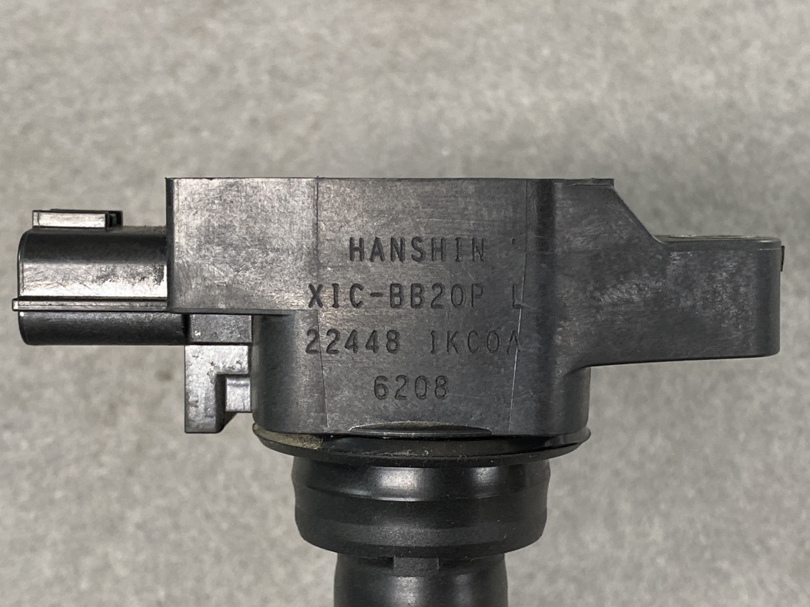 NIS-COIL-1KC0A_2 NISSAN RENAULT Genuine IGNITION COIL 22448 1KC0A / MR, QR Engine » NZ.95 » JDM-PARTS NZ » JDM-PARTS NZ Close-up of a dark pistol component with stamped markings: HANSHIN and other characters on a black metal surface against a gray background. NISSAN RENAULT Genuine IGNITION COIL 22448 1KC0A / MR, QR Engine » JDM-PARTS NZ