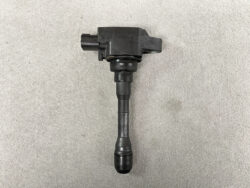 Automotive ignition coil with spark plug boot on a gray surface.