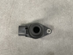 Close-up of a black plastic automotive sensor/connector with a circular port and a metal mounting hole on the right side.