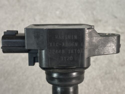 Close-up of a black plastic automotive sensor housing mounted on a shaft, with engraved serial numbers visible on the side.