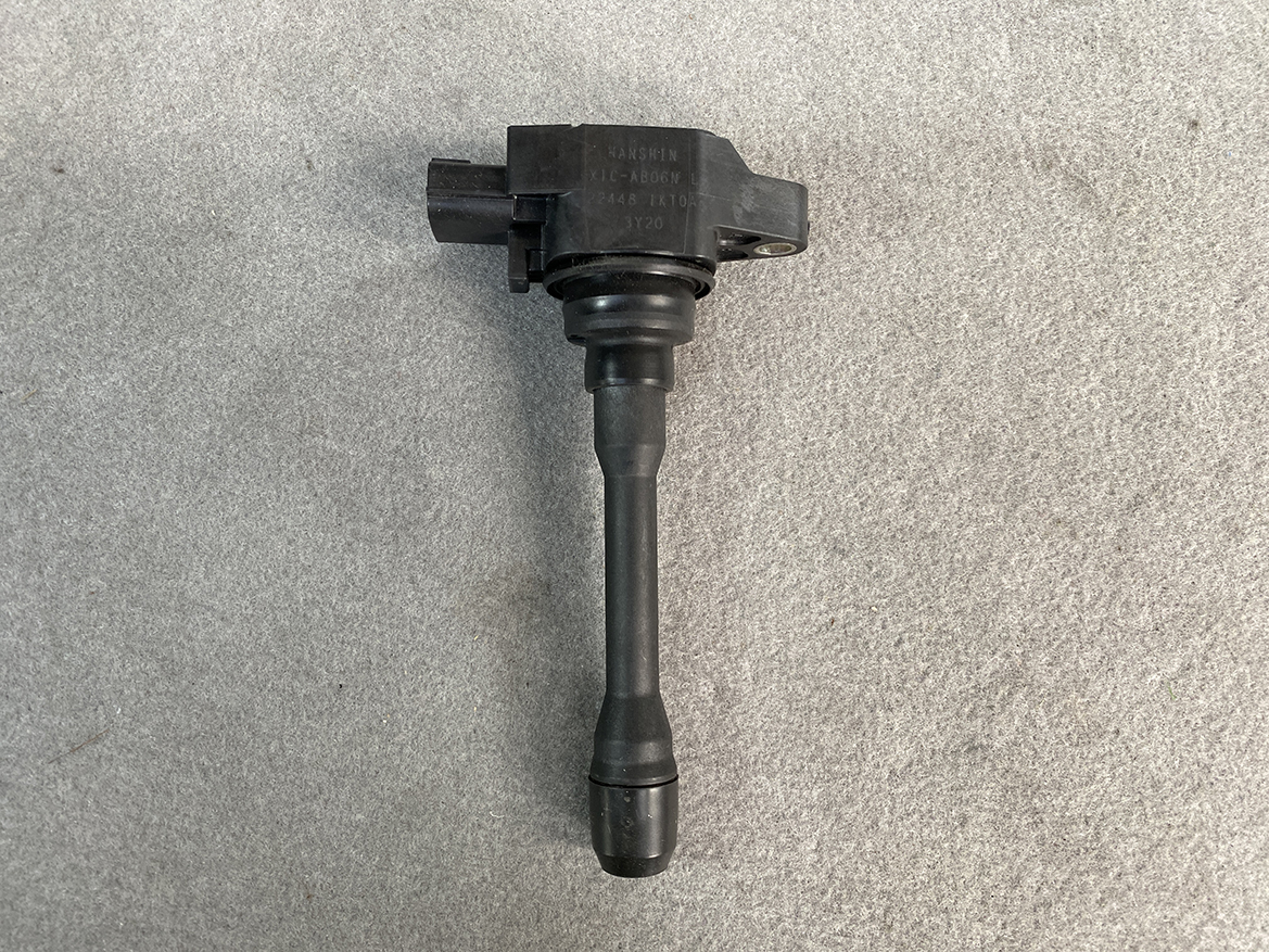 NIS-COIL-1KT0A_4 NISSAN Genuine Ignition Coil 22448 1KT0A / HR, MR, QR Engine » NZ.95 » JDM-PARTS NZ » JDM-PARTS NZ Black ignition coil with a rubber boot and electrical connector, laid on a gray surface (car engine part). NISSAN Genuine Ignition Coil 22448 1KT0A / HR, MR, QR Engine » JDM-PARTS NZ