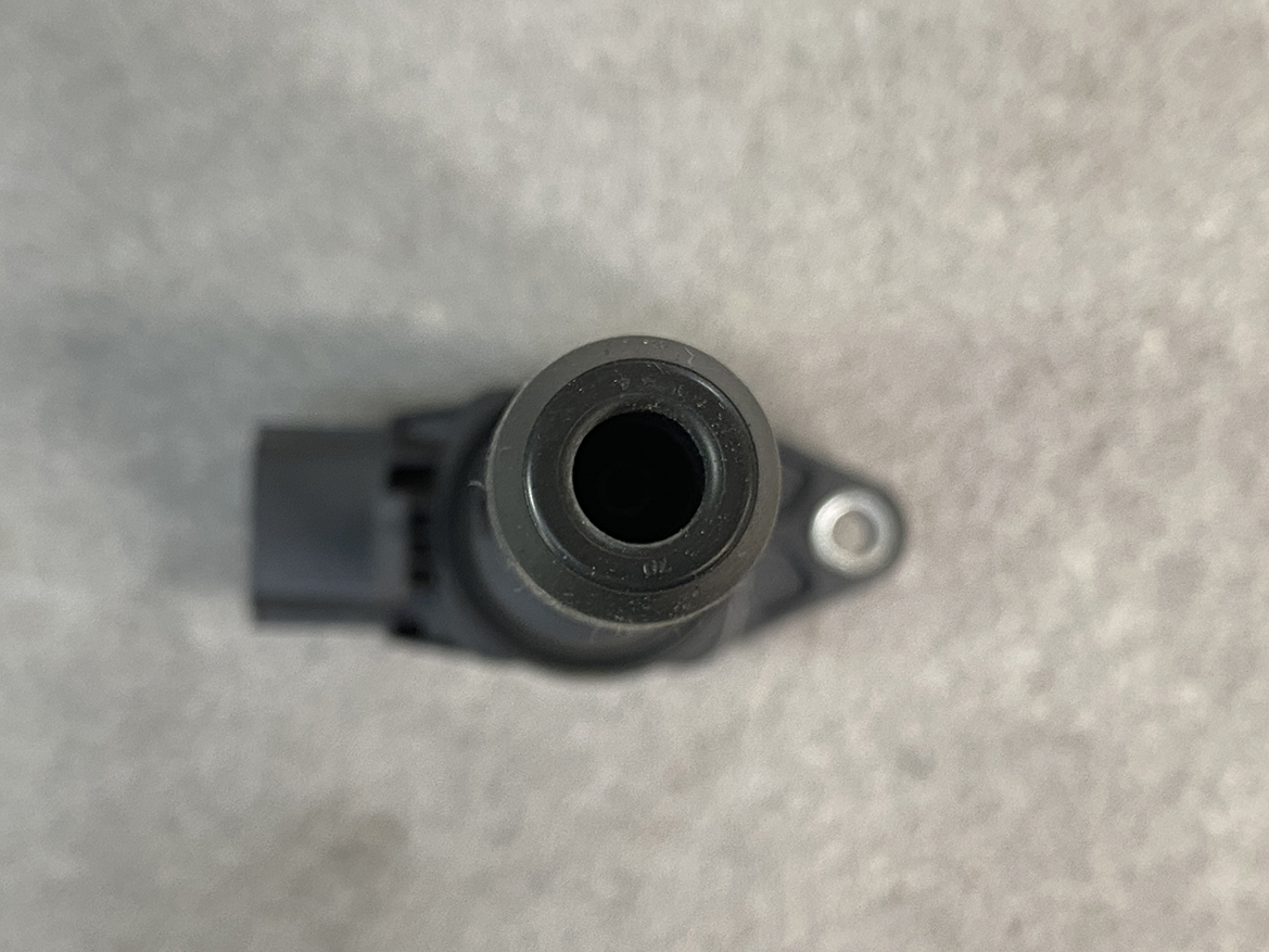 NIS-COIL-1KT0A_5 NISSAN Genuine Ignition Coil 22448 1KT0A / HR, MR, QR Engine » NZ.95 » JDM-PARTS NZ » JDM-PARTS NZ Top-down view of a small black cylindrical connector or nozzle with a hollow center, mounted to a bracket on a gray surface. NISSAN Genuine Ignition Coil 22448 1KT0A / HR, MR, QR Engine » JDM-PARTS NZ