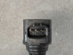 Close-up of a black automotive 3-pin connector with two visible metal contacts and numbering 6 and 7 on the receptacle edge, mounted to a gray housing — the connector's front view for wiring.