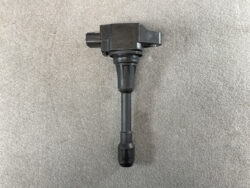 Ignition coil with rubber boot and electrical connector on a gray surface (auto part)