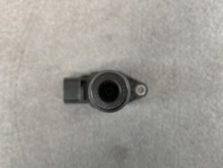 Top-down view of a black cylindrical connector with a hollow center on a small mounting arm on a gray surface.