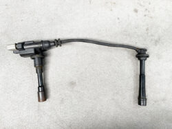Automotive ignition coil pack with a spark plug wire connected, lying on a concrete floor.