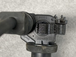 Close-up of a Denso automotive part with a black adjustment clamp and hose attached, viewed from above.