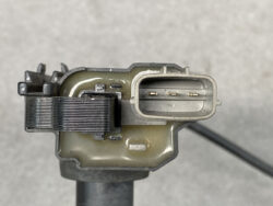 Close-up of an automotive sensor with a three-pin electrical connector and a metal housing, photographed from the side.