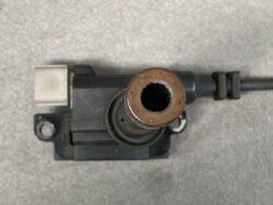 Top-down view of a copper-colored tube fitting protruding from a black plastic valve body on a gray surface.