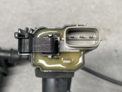 Close-up of an automotive electrical connector showing a rectangular pin housing with three gold pins, surrounded by greasy, greenish insulation material and a black ribbed mating surface nearby.