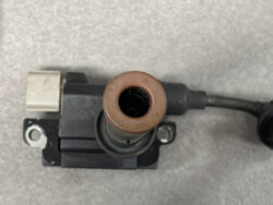 Ignition coil with brown rubber boot removed, exposing the hollow bore where the spark plug sits and a gray electrical connector on the left.