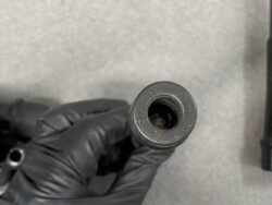 Close-up of a gloved hand holding a small black plastic connector with an internally threaded bore.