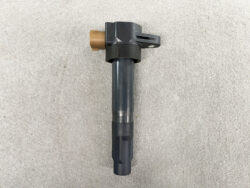 Automotive fuel injector with a brown electrical connector and mounting tab, lying on a concrete surface.