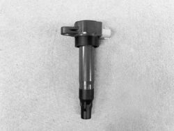 Automotive fuel injector lying on a gray surface, showing metal body and plastic nozzle at the bottom.