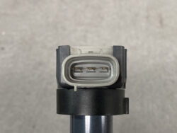 Close-up of a gray oval automotive electrical connector with three gold pins inside.