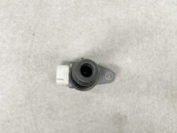 Close-up of a small round camera lens in a black housing mounted on a gray bracket, viewed from above on a concrete surface.