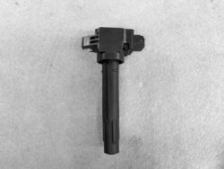 Automotive ignition coil with rectangular top and long cylindrical body on a gray surface