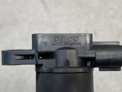 Close-up of a black plastic DENSO automotive component with the engraving 'DENSO MADE IN JAPAN' visible, mounted on a cylindrical surface.