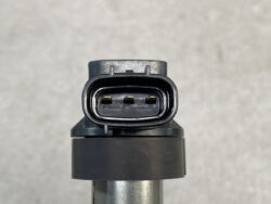 Close-up of a three-pin automotive electrical connector with a black plastic housing, mounted on a metallic rod against a gray background.